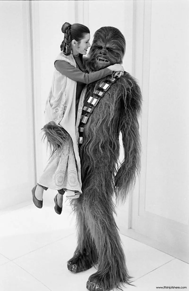 Carrie is lifted by co-star and Wookie, Peter Mayhew, while filming.
